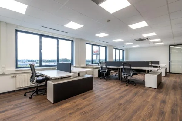 Moderne, licht ingerichte kantoorruimte met bureaus, bureaustoelen en grote ramen.