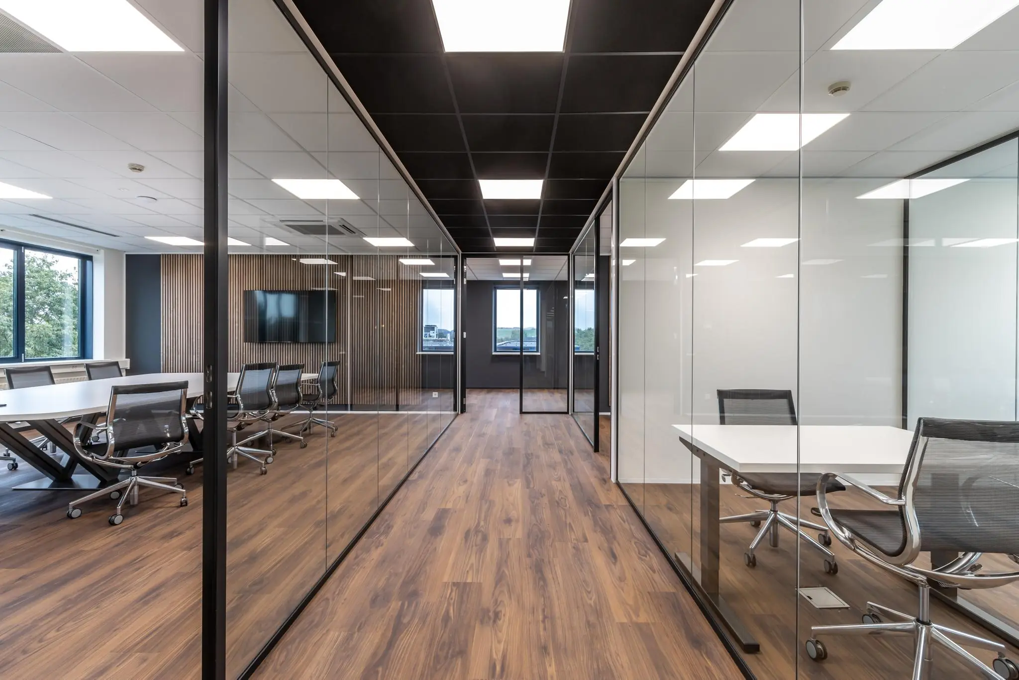 Moderne kantoorruimte met glazen wanden, houten vloer en vergadertafels met bureaustoelen.