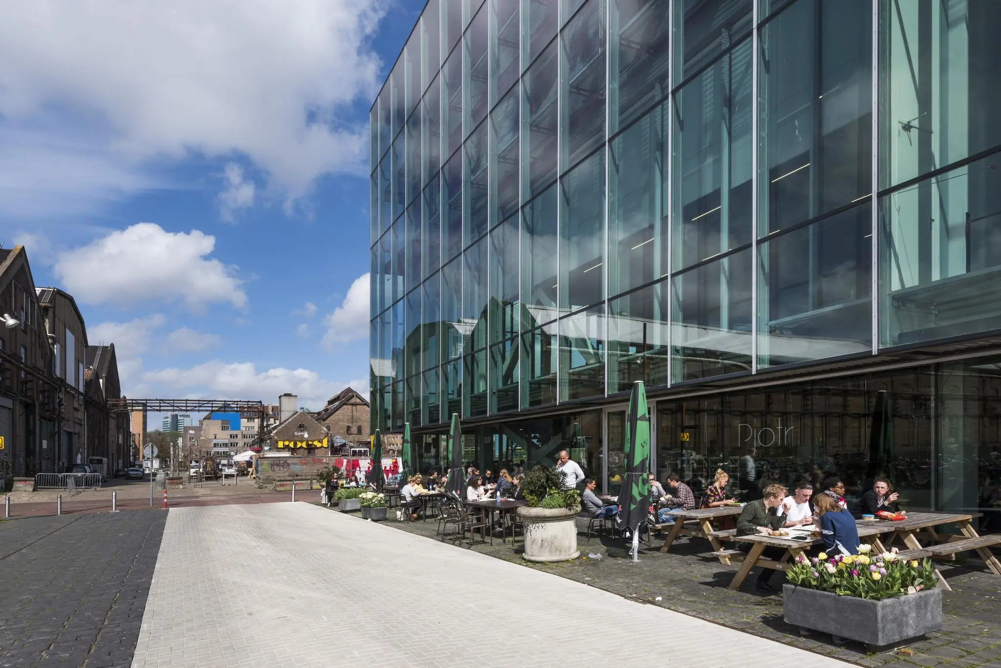 Terras met etende mensen naast een modern glazen gebouw aan de Jacob Bontiusplaats in Amsterdam.
