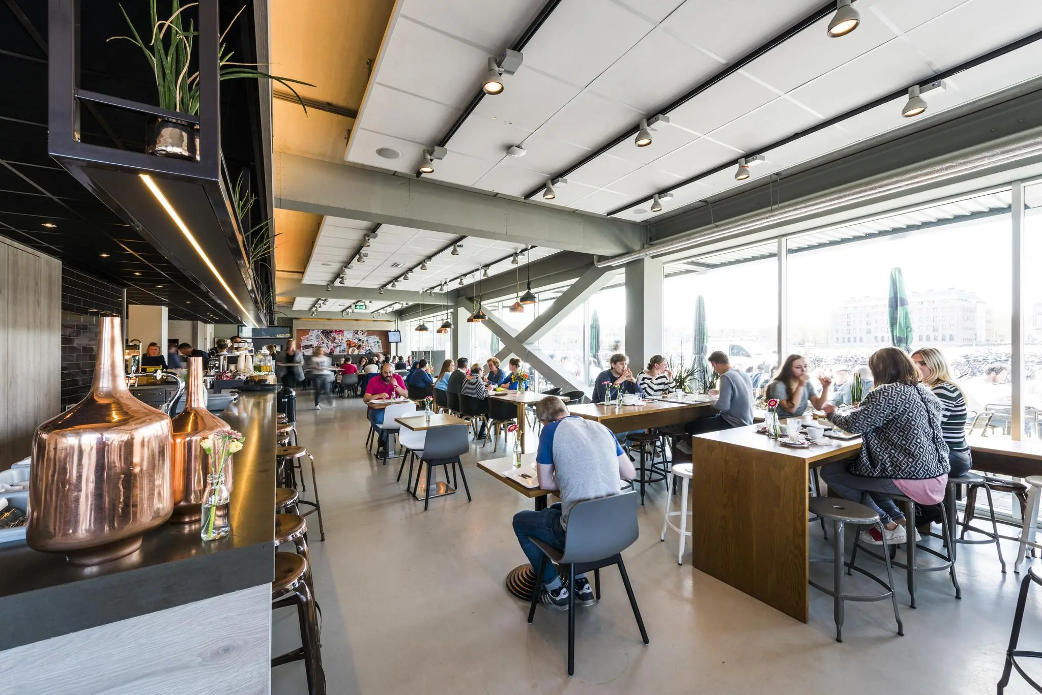 Modern en licht restaurant aan de Jacob Bontiusplaats met mensen die aan lange tafels eten en praten.