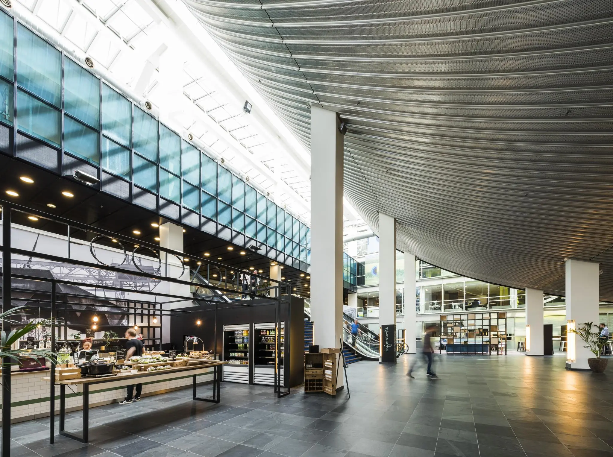 Licht en modern interieur van het gebouw aan de Jacob Bontiusplaats met een open horecapunt en roltrappen in het atrium.
