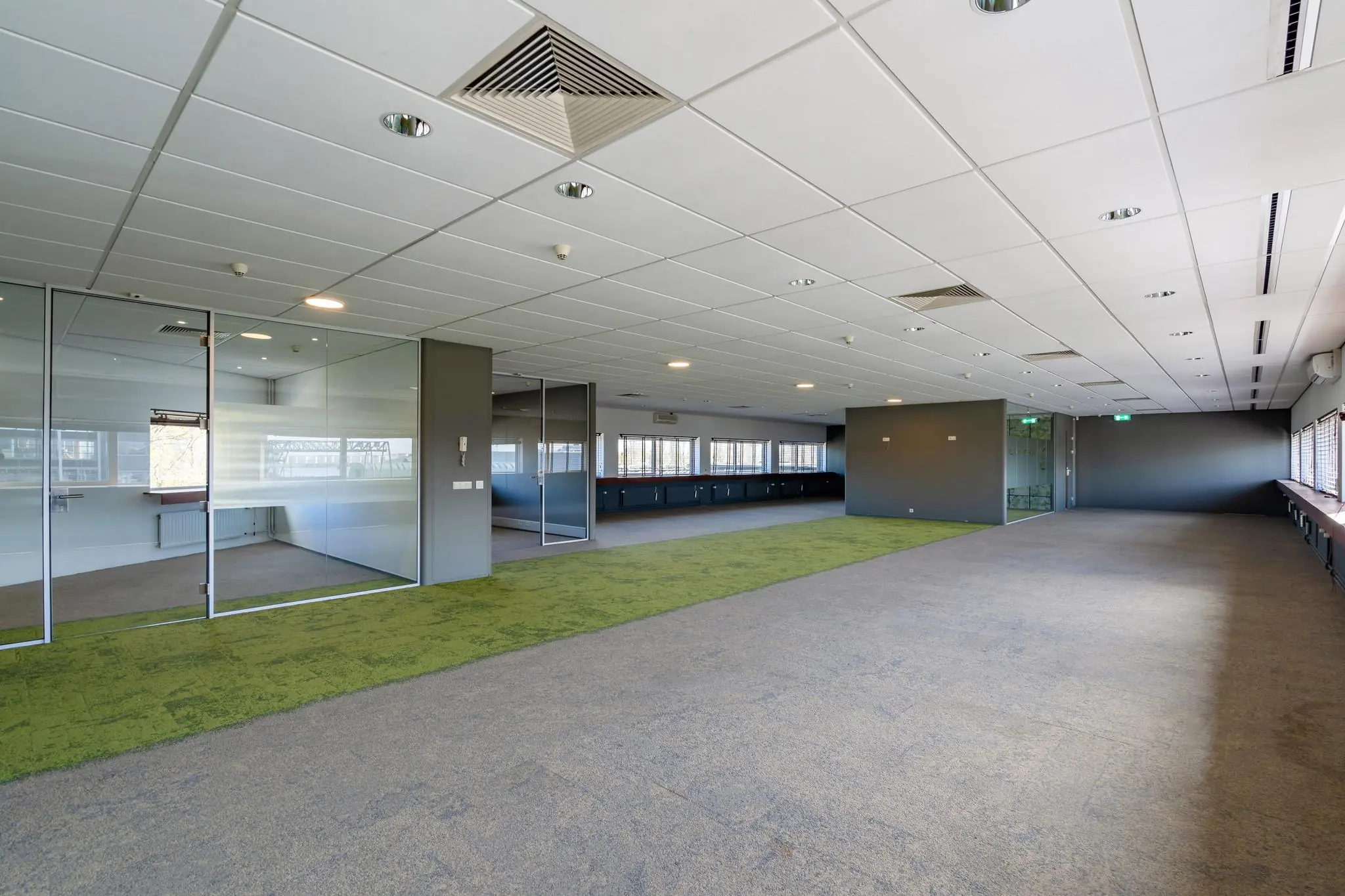 Moderne, lege kantoorruimte aan de Mijlweg met glazen vergaderruimtes en grijs-groen tapijt.