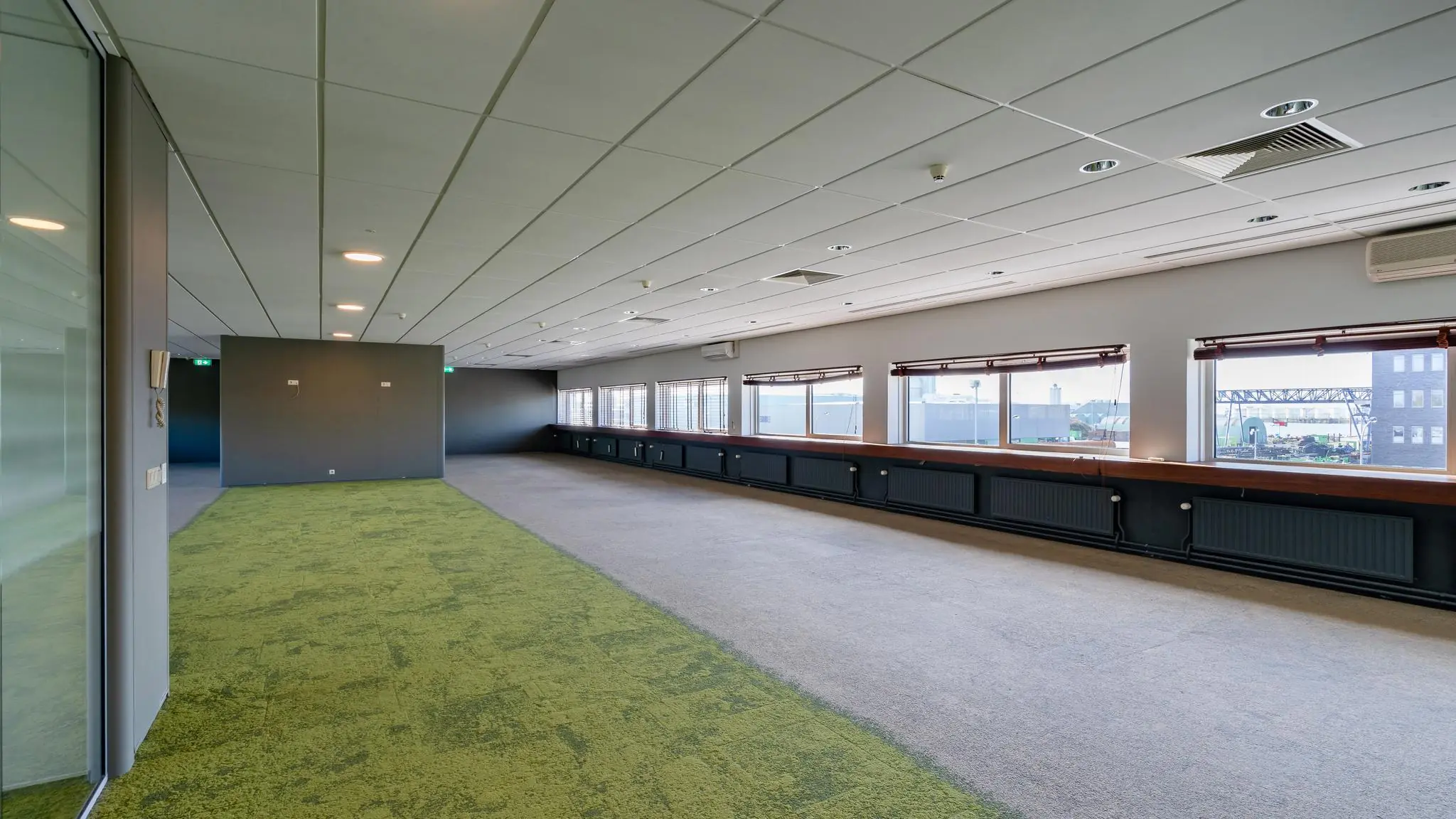 Ruime, lege kantoorruimte aan de Mijlweg met grote ramen en deels groen tapijt.