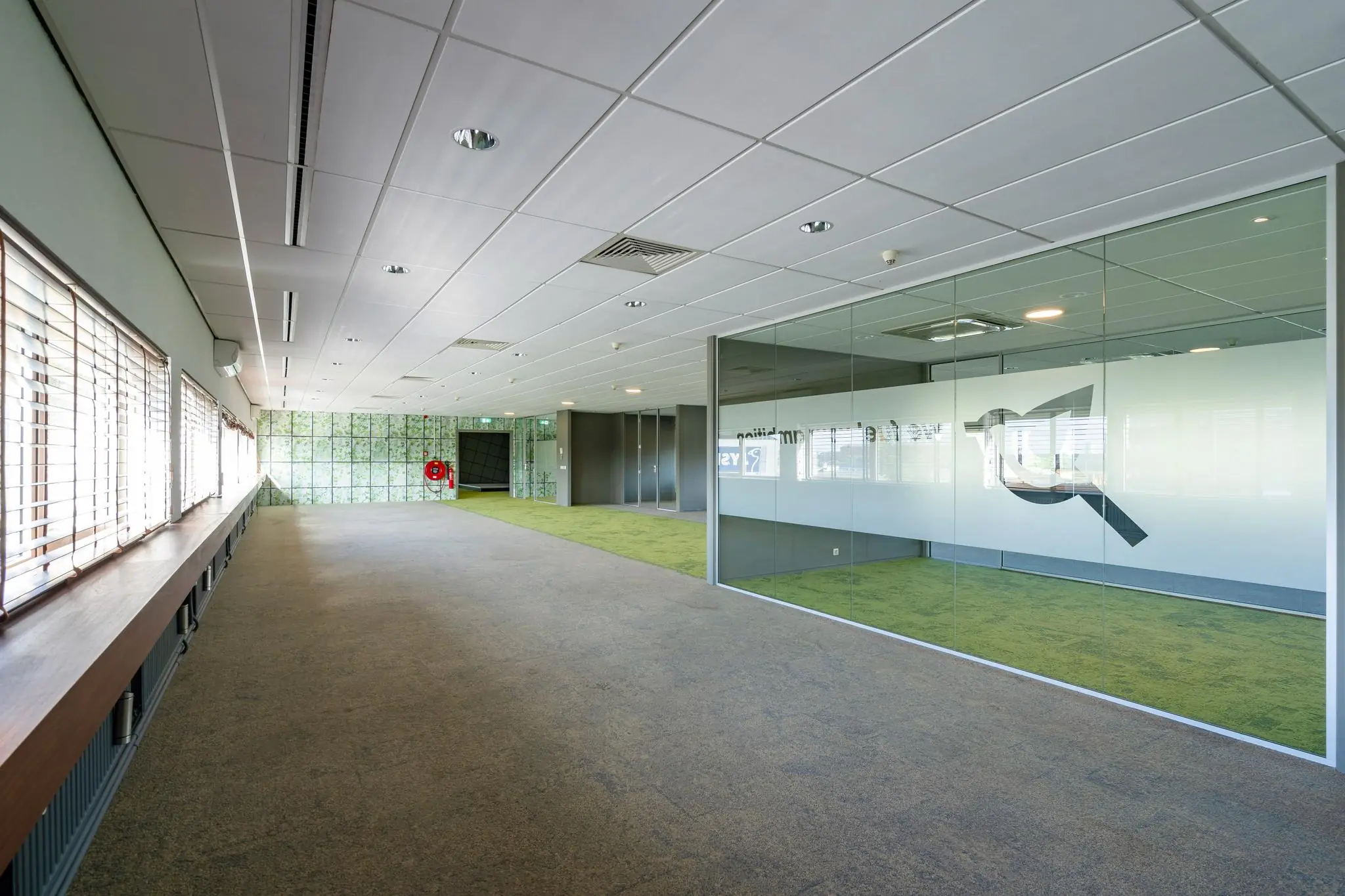 Ruime, moderne kantoorruimte aan de Mijlweg met glazen vergaderruimte en groene vloerbedekking.
