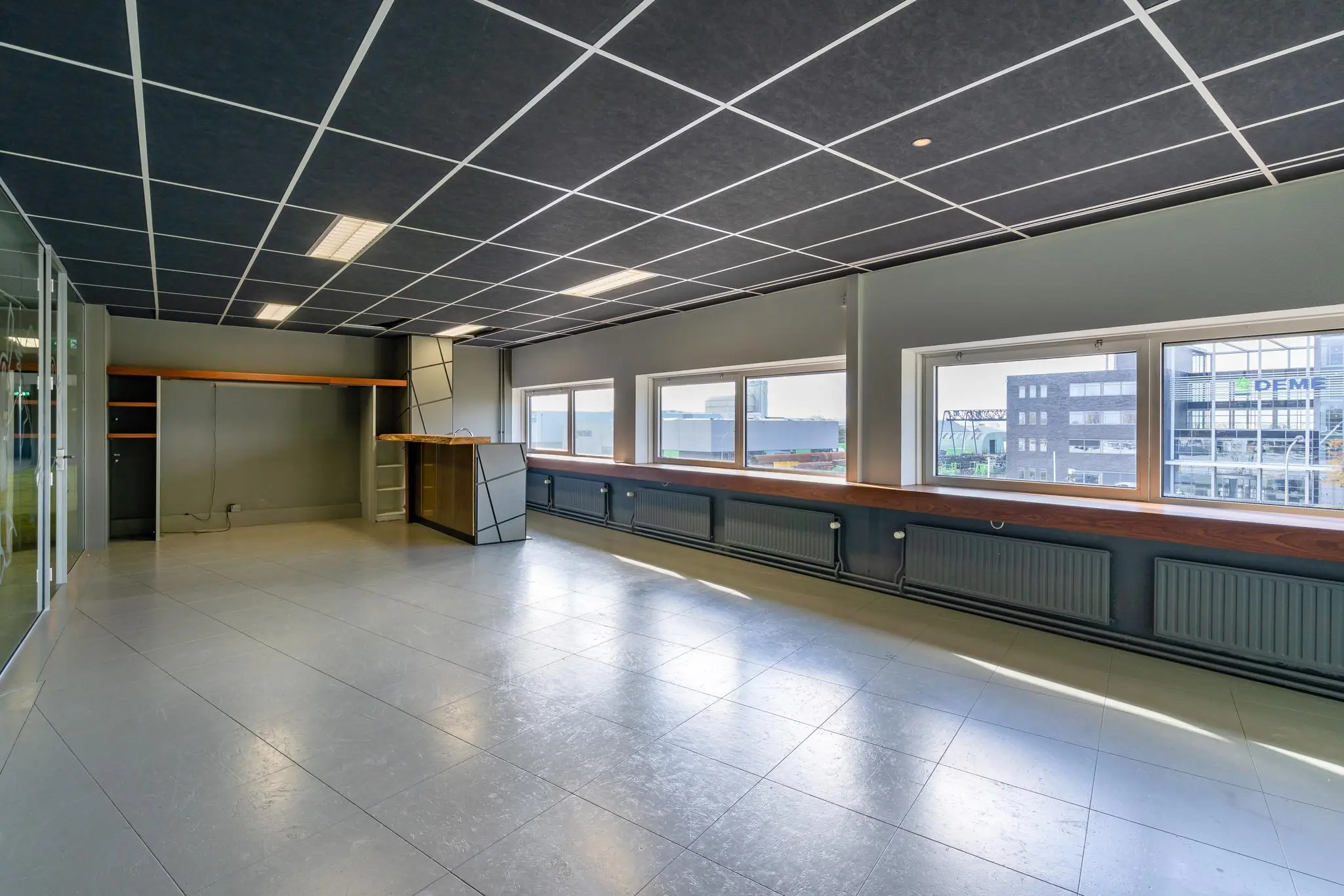 Lichte kantoorruimte aan de Mijlweg met grote ramen, een bar en moderne plafondafwerking.