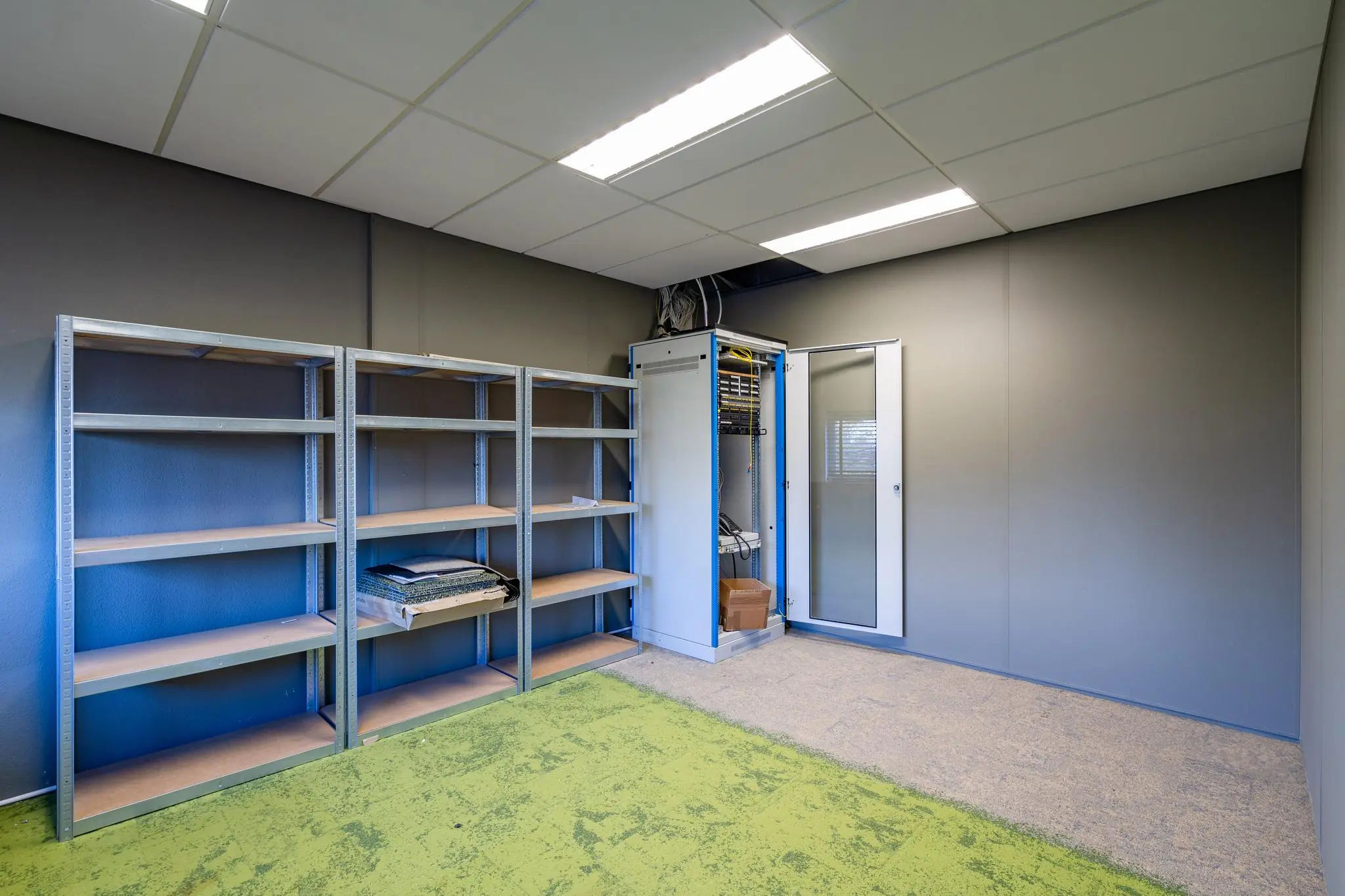 Een lege technische ruimte met metalen stellingen en een open serverkast aan de Mijlweg.