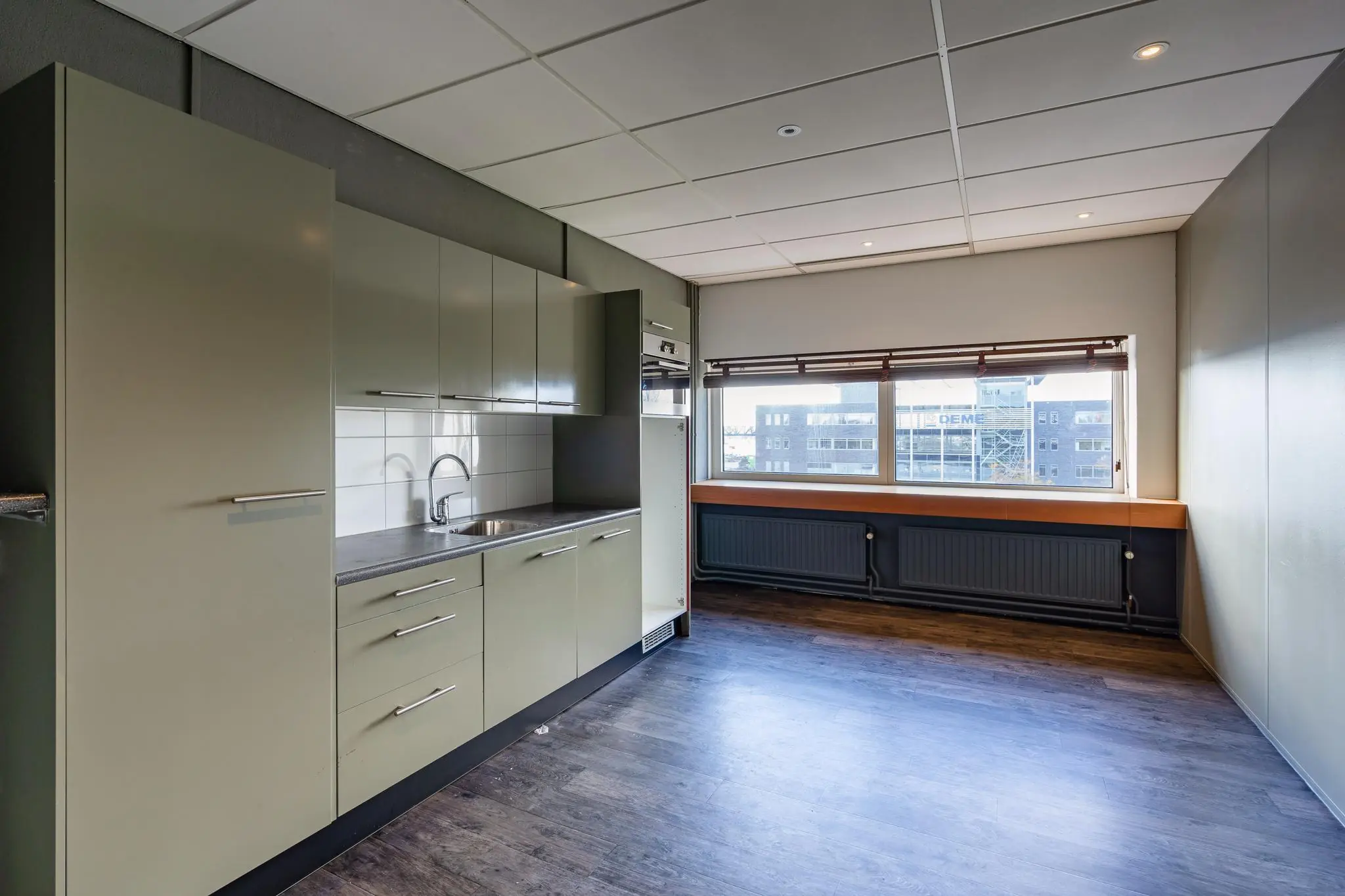 Moderne keukenruimte met lichtgroene kasten, een donker aanrechtblad en een groot raam met uitzicht op bedrijventerrein aan de Mijlweg.