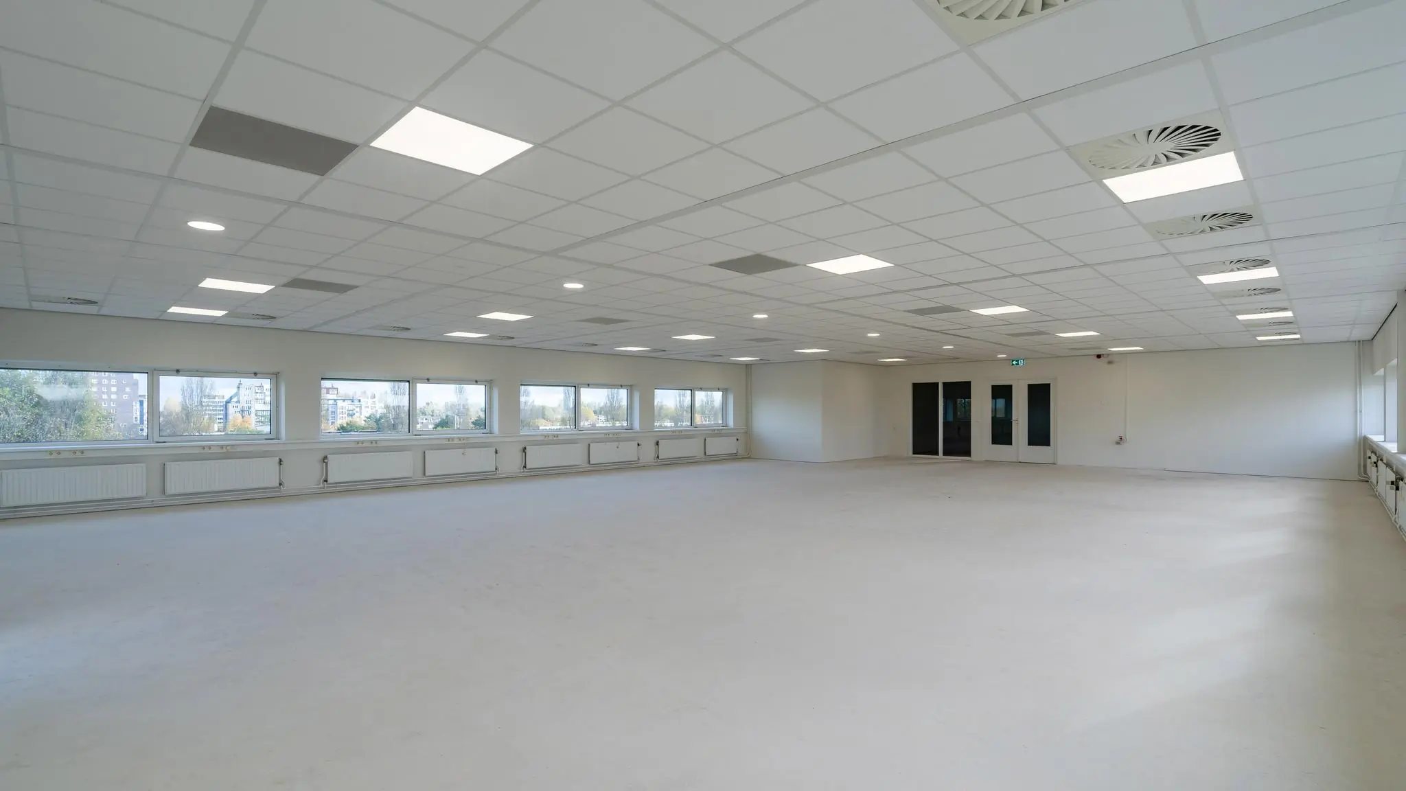 Lichte, lege kantoorruimte aan de Mijlweg met systeemplafond, grote ramen en witte muren.