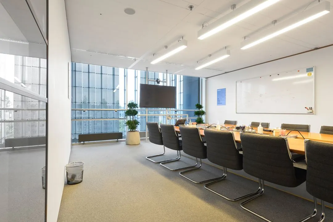 Vergaderruimte met lange tafel, moderne stoelen, whiteboard, groot scherm en uitzicht op de gevel van het gebouw aan de Jacob Bontiusplaats.