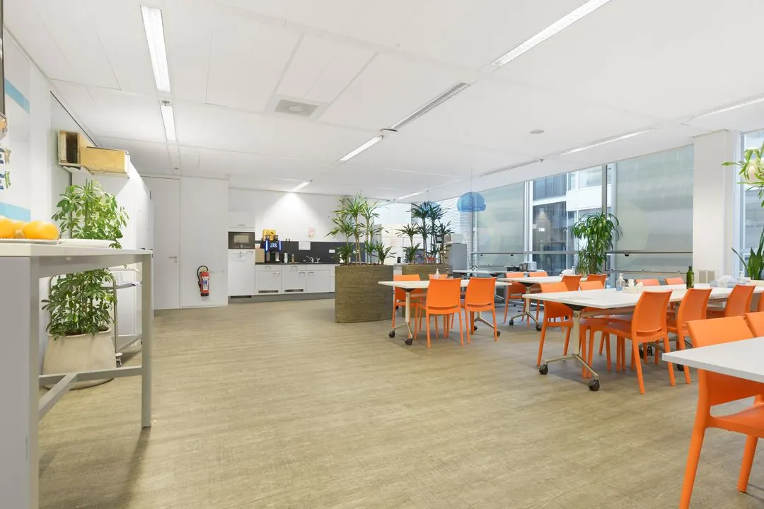 Moderne bedrijfskeuken en kantine met oranje stoelen, witte tafels en veel groen op Jacob Bontiusplaats.