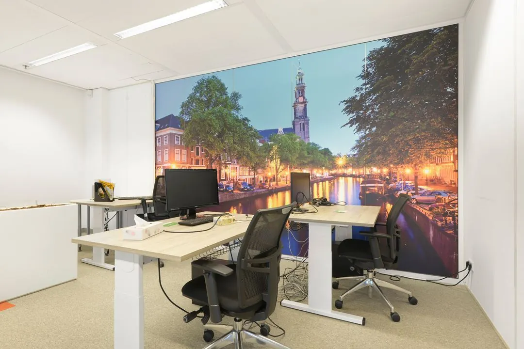 Modern kantoor met zit-sta bureaus en een grote wandfoto van de Amsterdamse Jacob Bontiusplaats met uitzicht op de Westertoren.