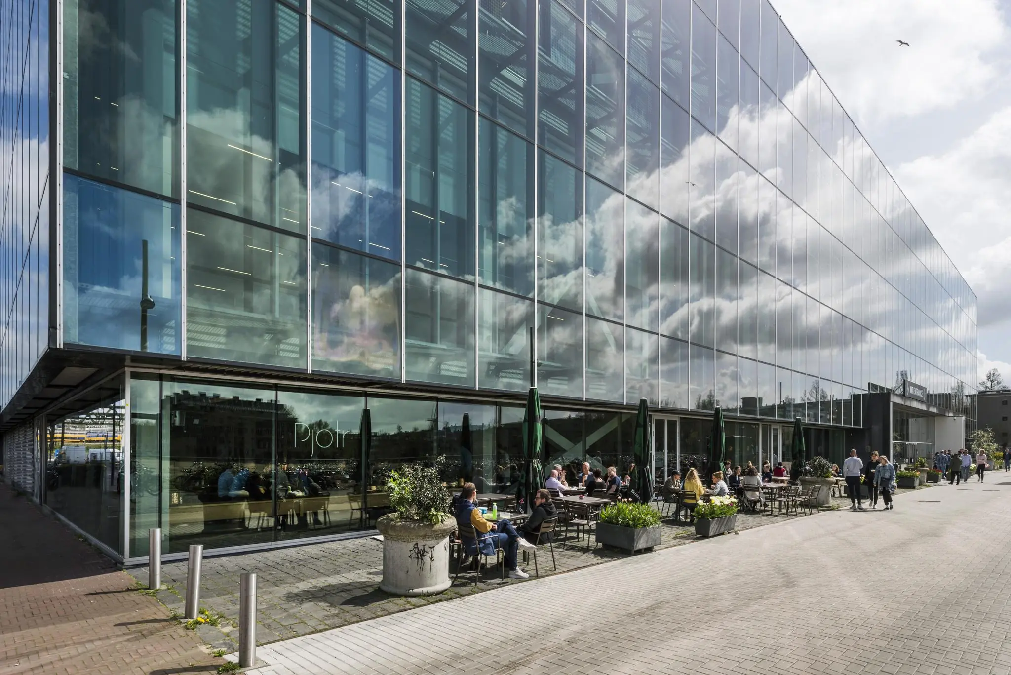 Terras aan de Jacob Bontiusplaats met mensen die zitten bij het glazen gebouw van restaurant Pjotr.