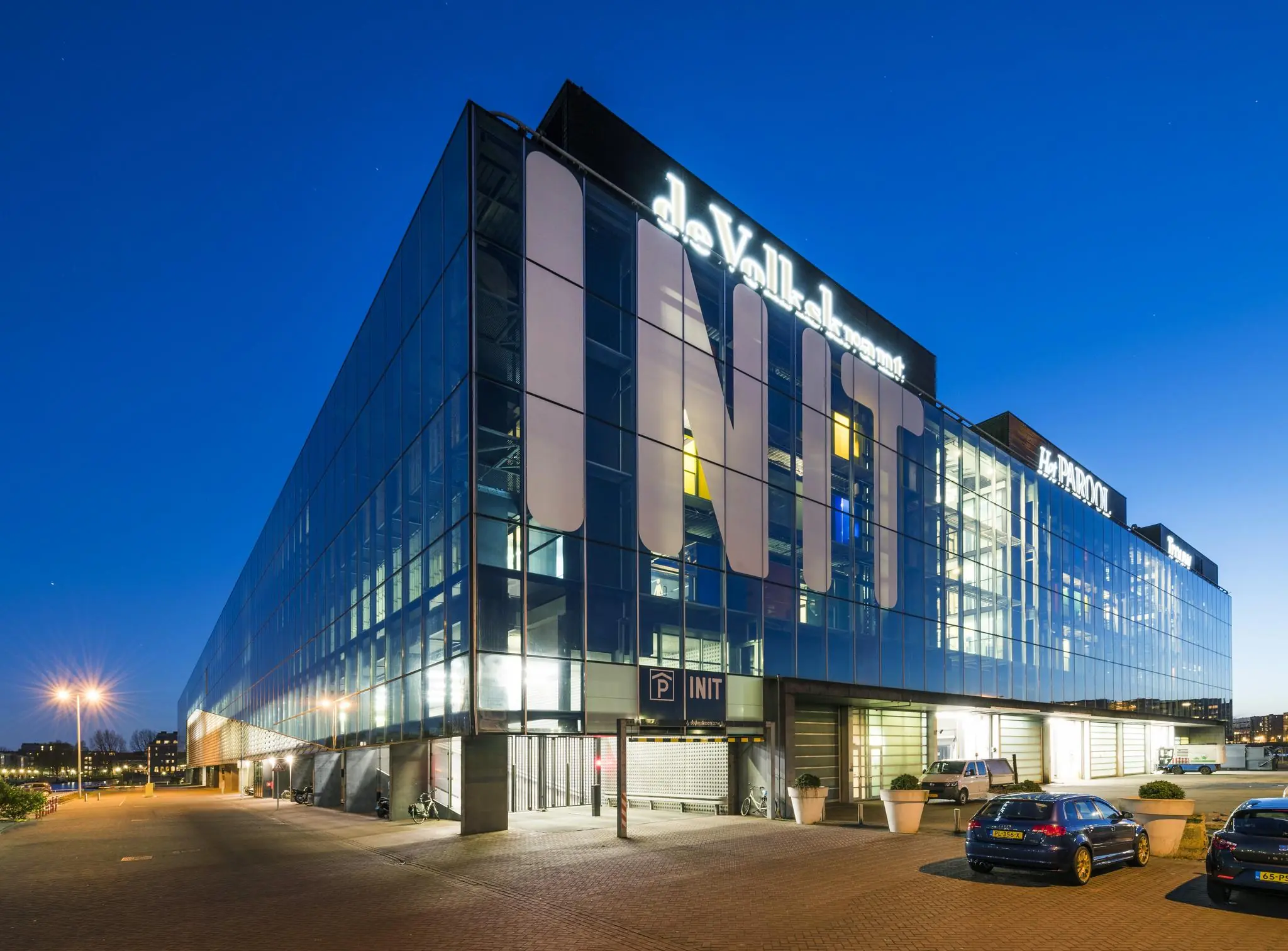 Modern kantoorcomplex INIT aan de Jacob Bontiusplaats in Amsterdam, 's avonds verlicht met zicht op de gevels van dagbladen als de Volkskrant en Het Parool.