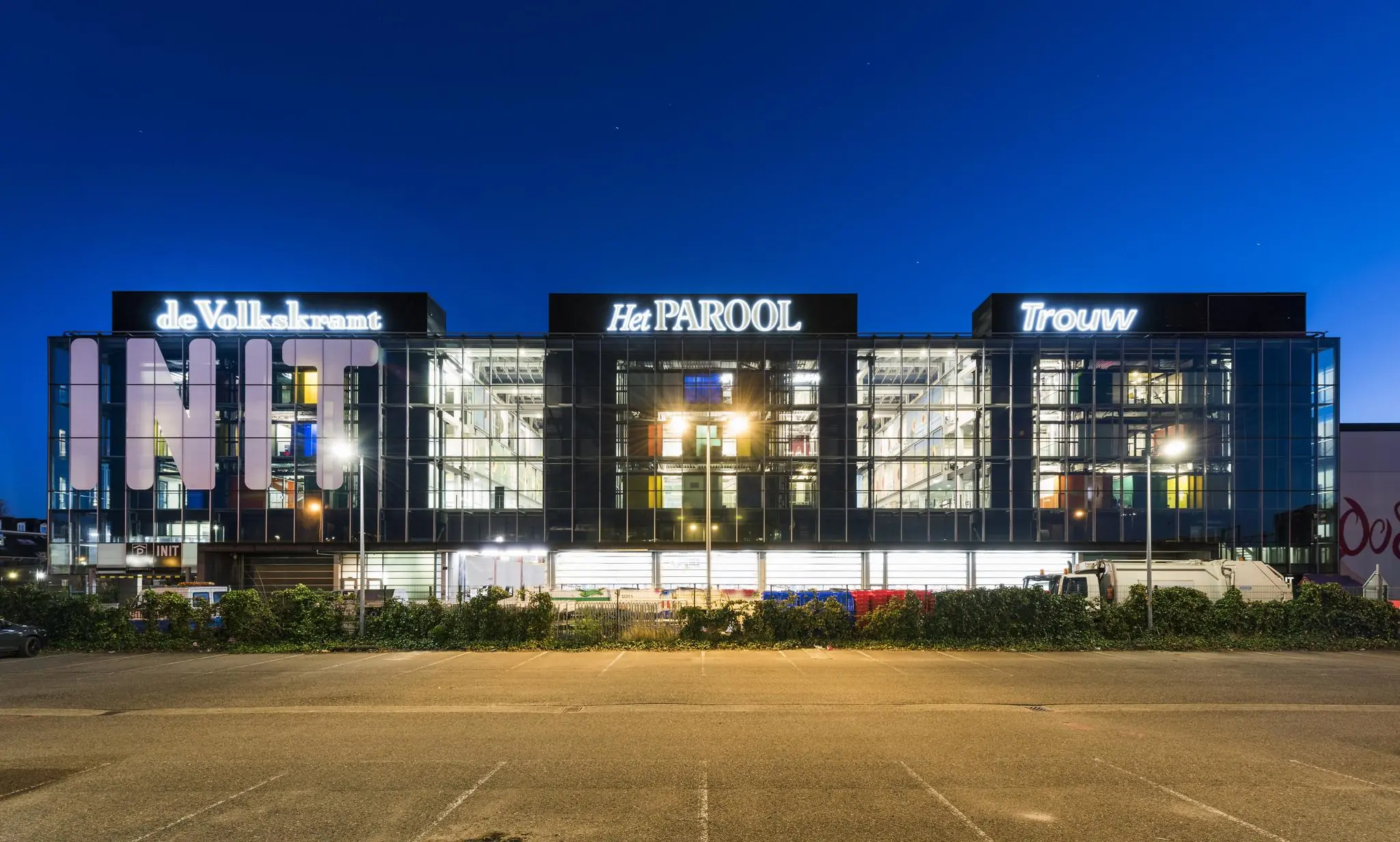 Verlicht kantoorgebouw INIT aan de Jacob Bontiusplaats in Amsterdam met de logo's van de kranten de Volkskrant, Het Parool en Trouw.