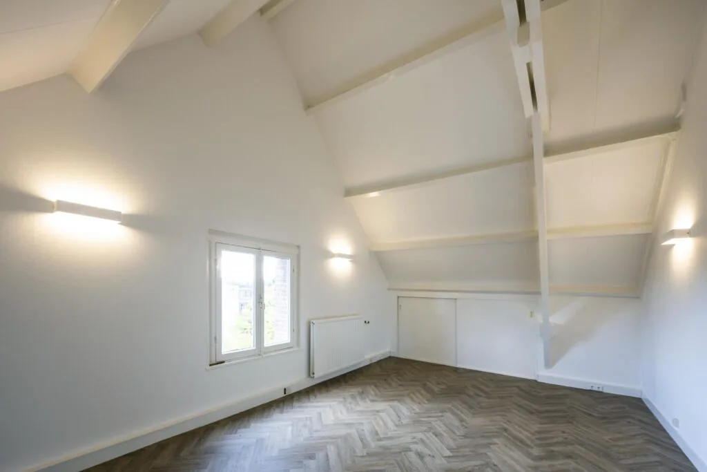 Lichte zolderkamer aan de Emmalaan met hoog plafond, houten visgraatvloer en witgeschilderde balken.
