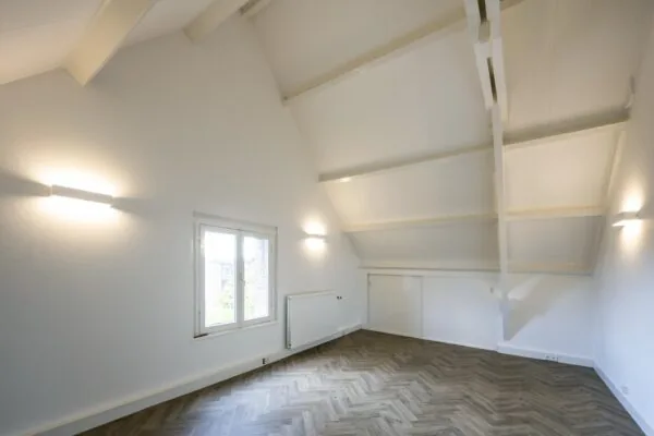Lichte zolderkamer aan de Emmalaan met hoog plafond, houten visgraatvloer en witgeschilderde balken.