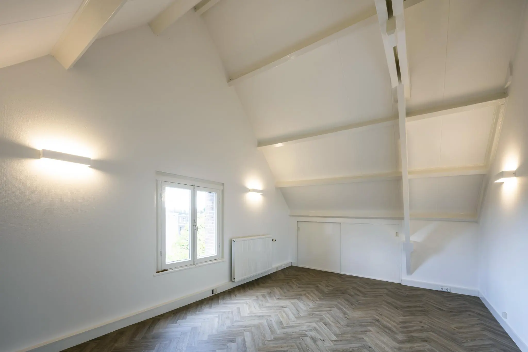Lichte zolderkamer aan de Emmalaan met hoog plafond, houten visgraatvloer en witgeschilderde balken.