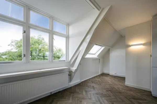 Lichte zolderkamer aan de Emmalaan met grote ramen, schuin dak en visgraatvloer.