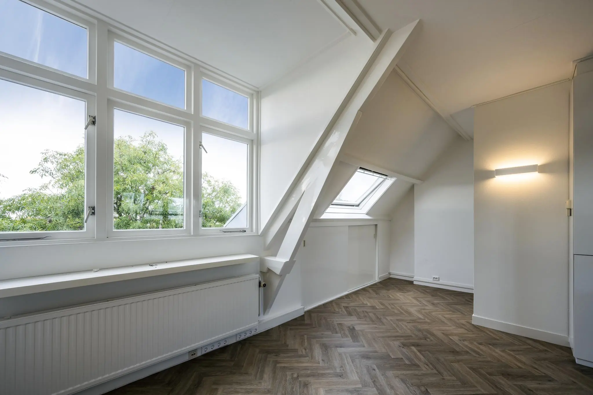 Lichte zolderkamer aan de Emmalaan met grote ramen, schuin dak en visgraatvloer.