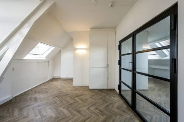 Lichte zolderruimte aan de Emmalaan met visgraatvloer, schuine dakkapel met dakraam en zwarte glazen binnendeuren.