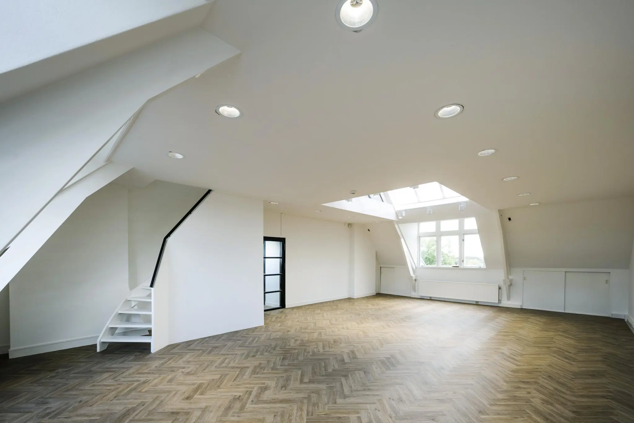 Lichte, ruime zolderkamer met visgraatvloer, dakramen en een witte trap aan de Emmalaan.