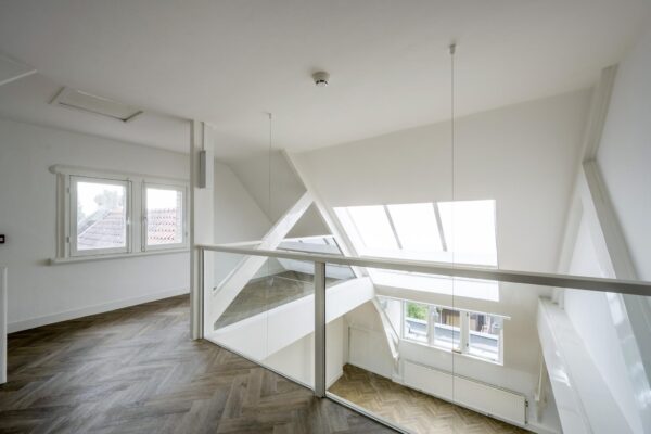Licht en modern ingericht split-level interieur met glazen balustrade en visgraat houten vloer aan de Emmalaan.