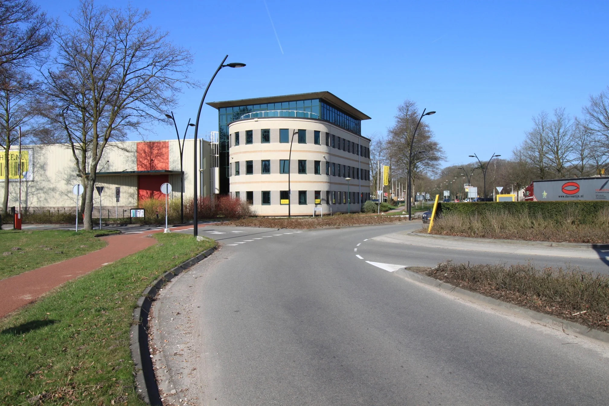 Moderne kantoorgebouw aan de Koningsweg met rotonde en vrachtverkeer op een zonnige dag.