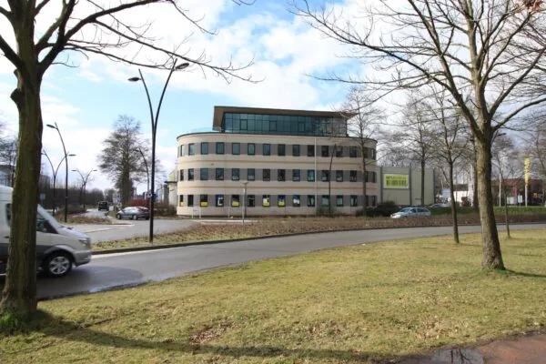 Kantoorpand aan de Koningsweg met ronde gevel en omringd door bomen en een rotonde.