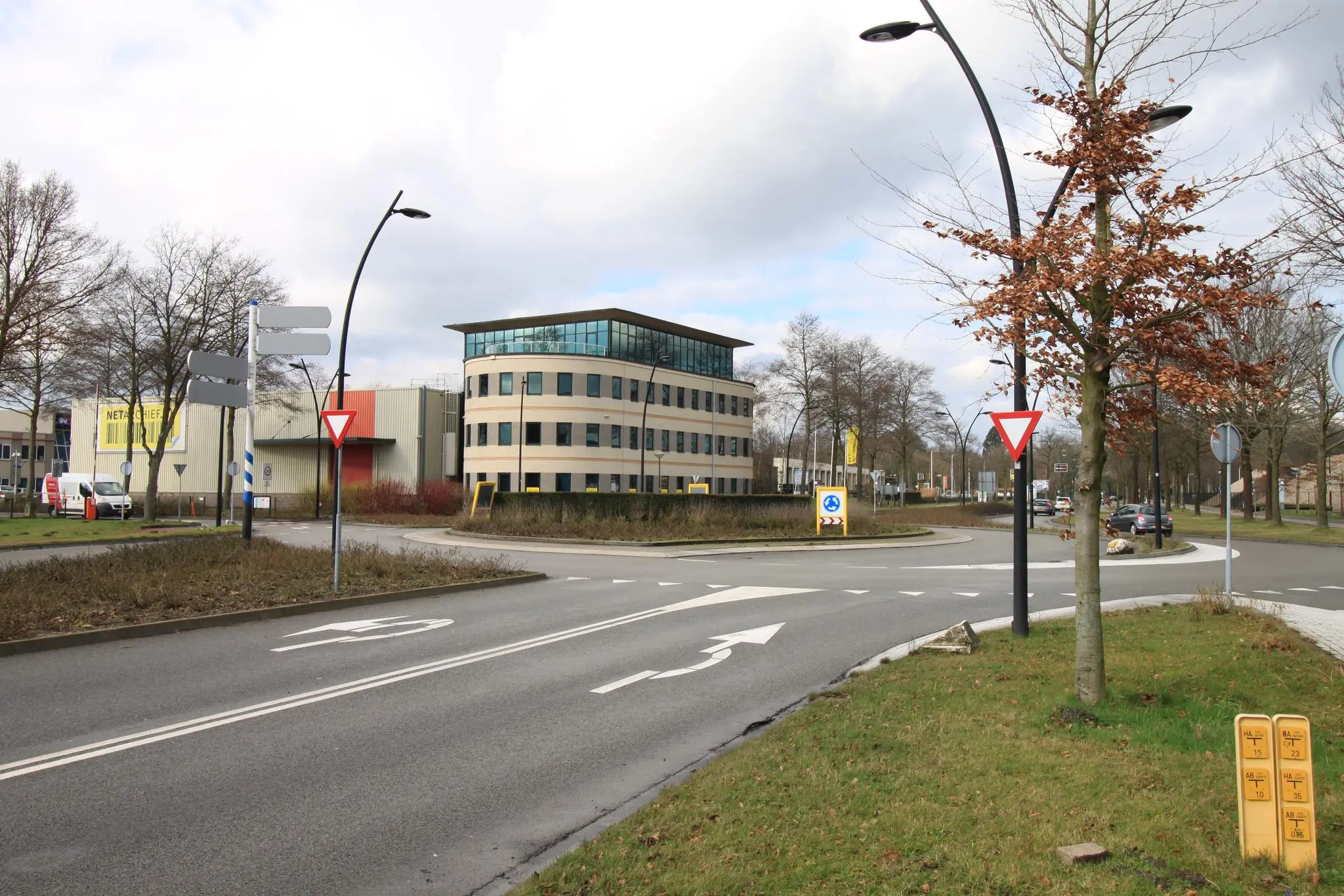 Rotonde aan de Koningsweg met kantoorgebouw en verkeersborden op een bewolkte dag.