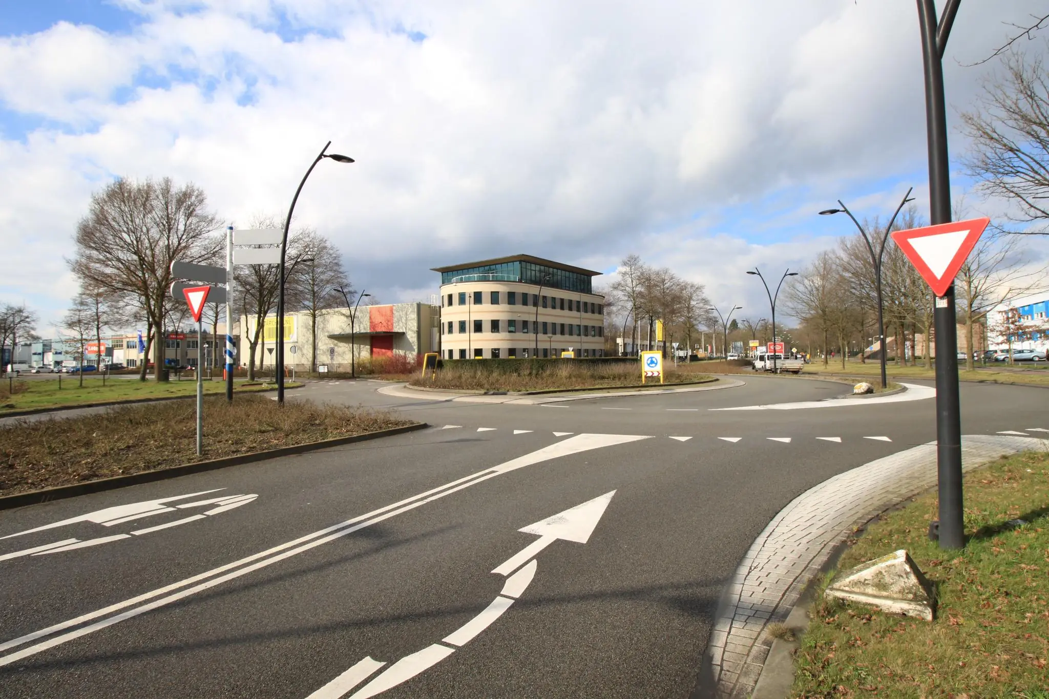 Rotonde op de Koningsweg met moderne kantoorgebouwen en verkeersborden onder een deels bewolkte lucht.