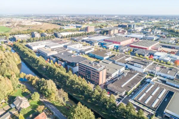 Luchtfoto van bedrijventerrein met kantoren, magazijnen en een waterkanaal omringd door bomen.