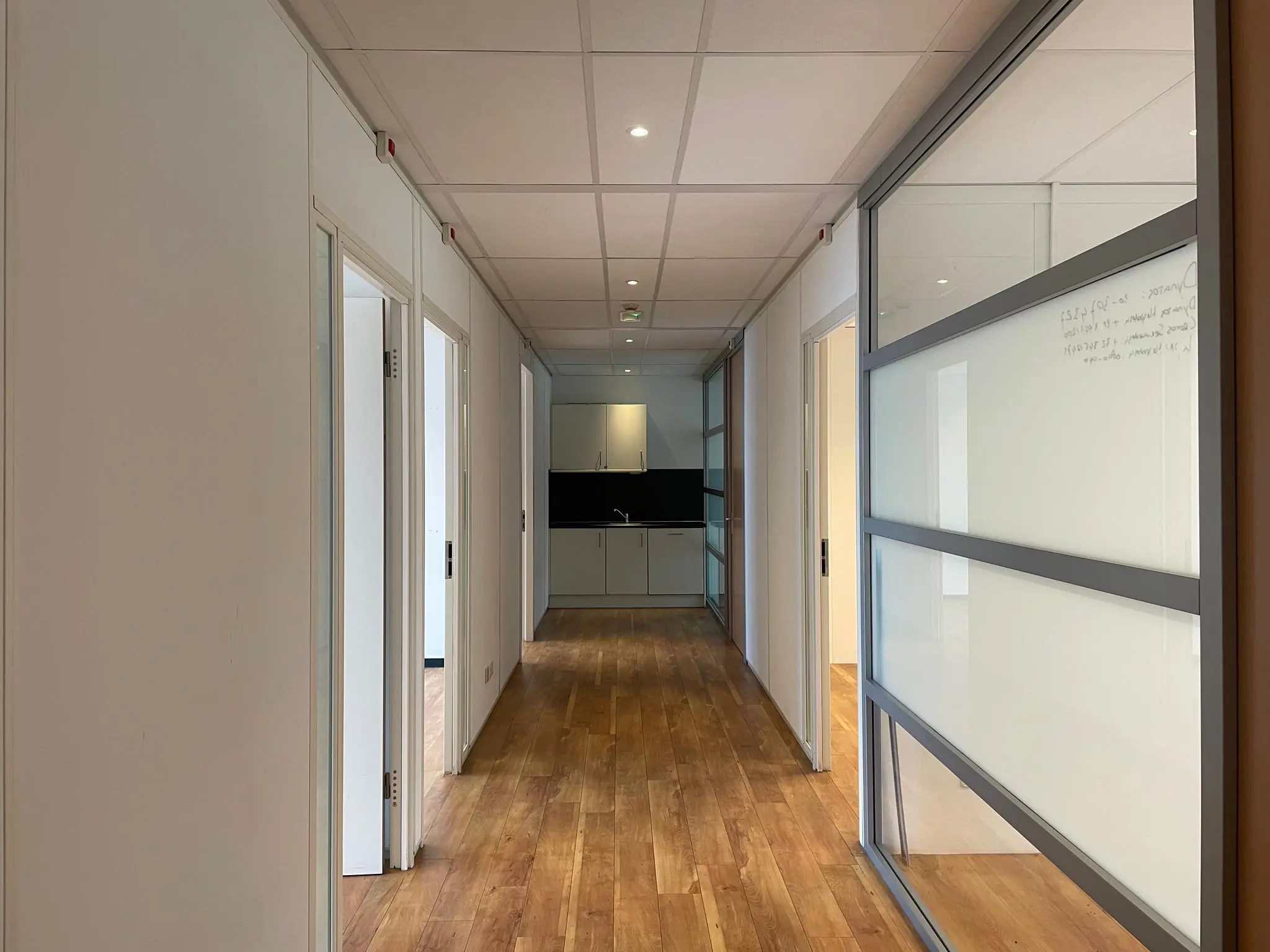 Moderne kantoorruimte met houten vloer, open deuren en een kitchenette aan het einde van de gang.