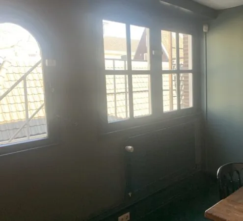 Zonlicht valt naar binnen door ramen met uitzicht op dakpannen aan de Leidsegracht.