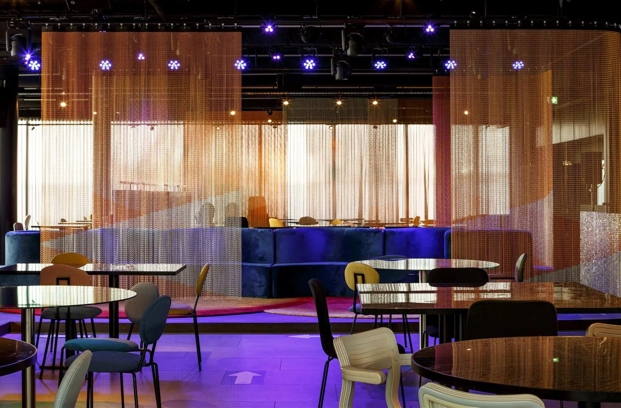 Moderne horecagelegenheid aan de Moermanskkade met sfeervolle verlichting, fluwelen zitbanken en metalen kralengordijnen als afscheiding.