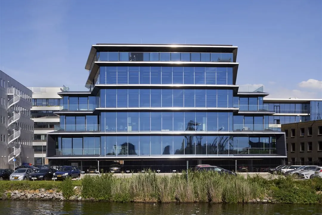 Modern kantoorgebouw met glazen gevel aan de Moermanskkade, gezien vanaf het water.