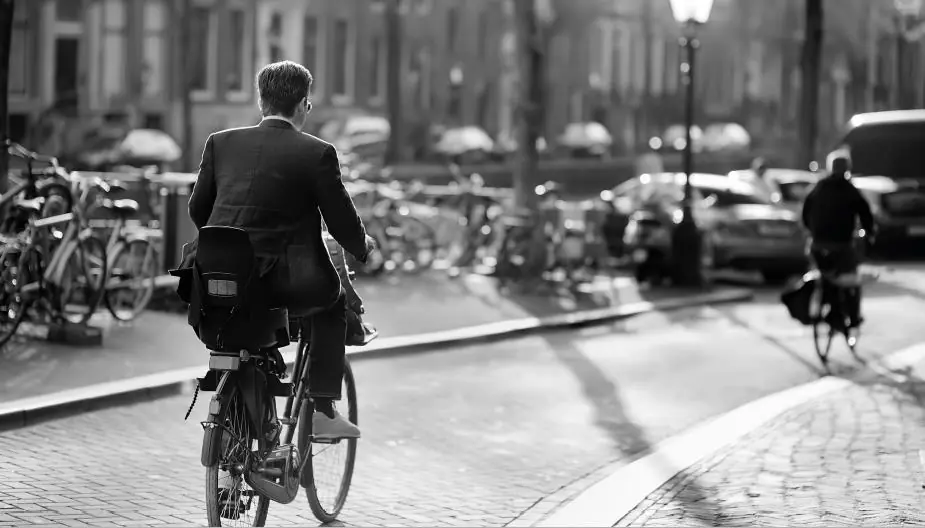 Man in pak fietst over de Reguliersdwarsstraat in Amsterdam op een zonnige dag.