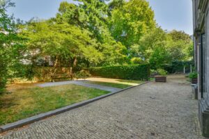 Ruime, groene stadstuin aan de Herengracht met grasveld, zitbank en omringende bomen.