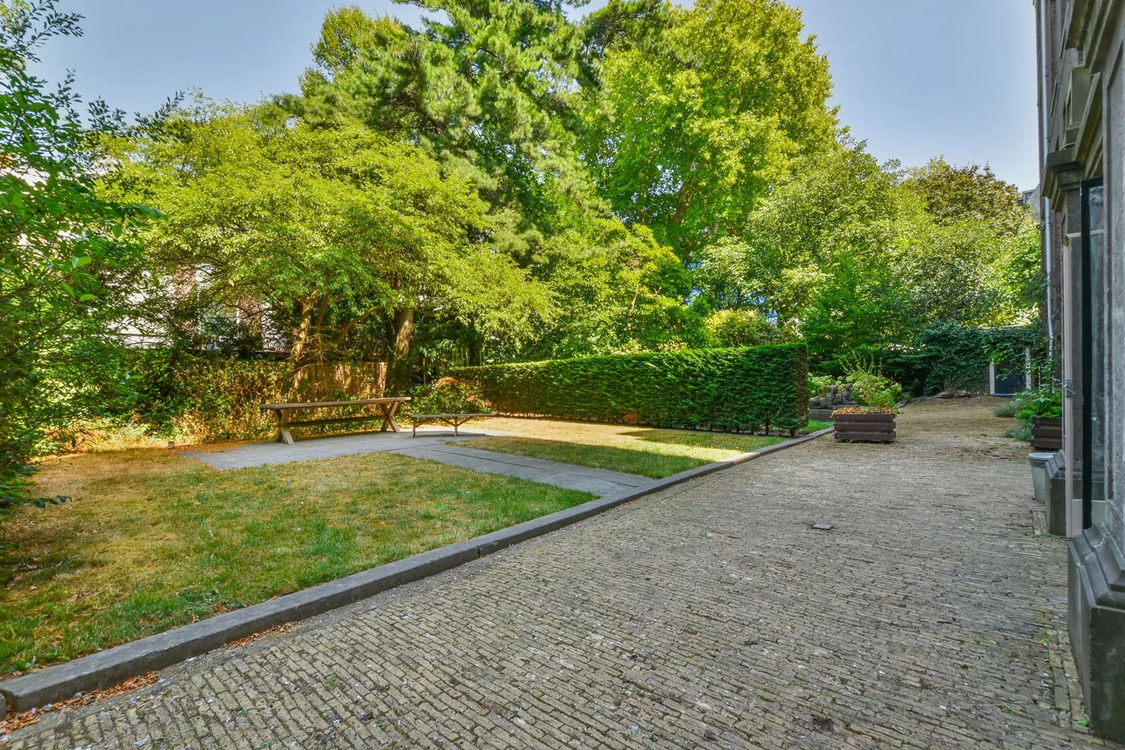 Ruime, groene stadstuin aan de Herengracht met grasveld, zitbank en omringende bomen.
