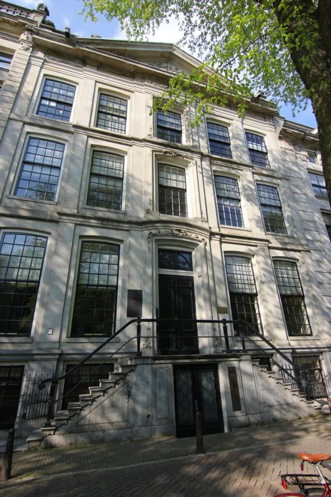 Voorgevel van een monumentaal grachtenpand aan de Herengracht in Amsterdam met hoge ramen en een dubbele trap naar de ingang.