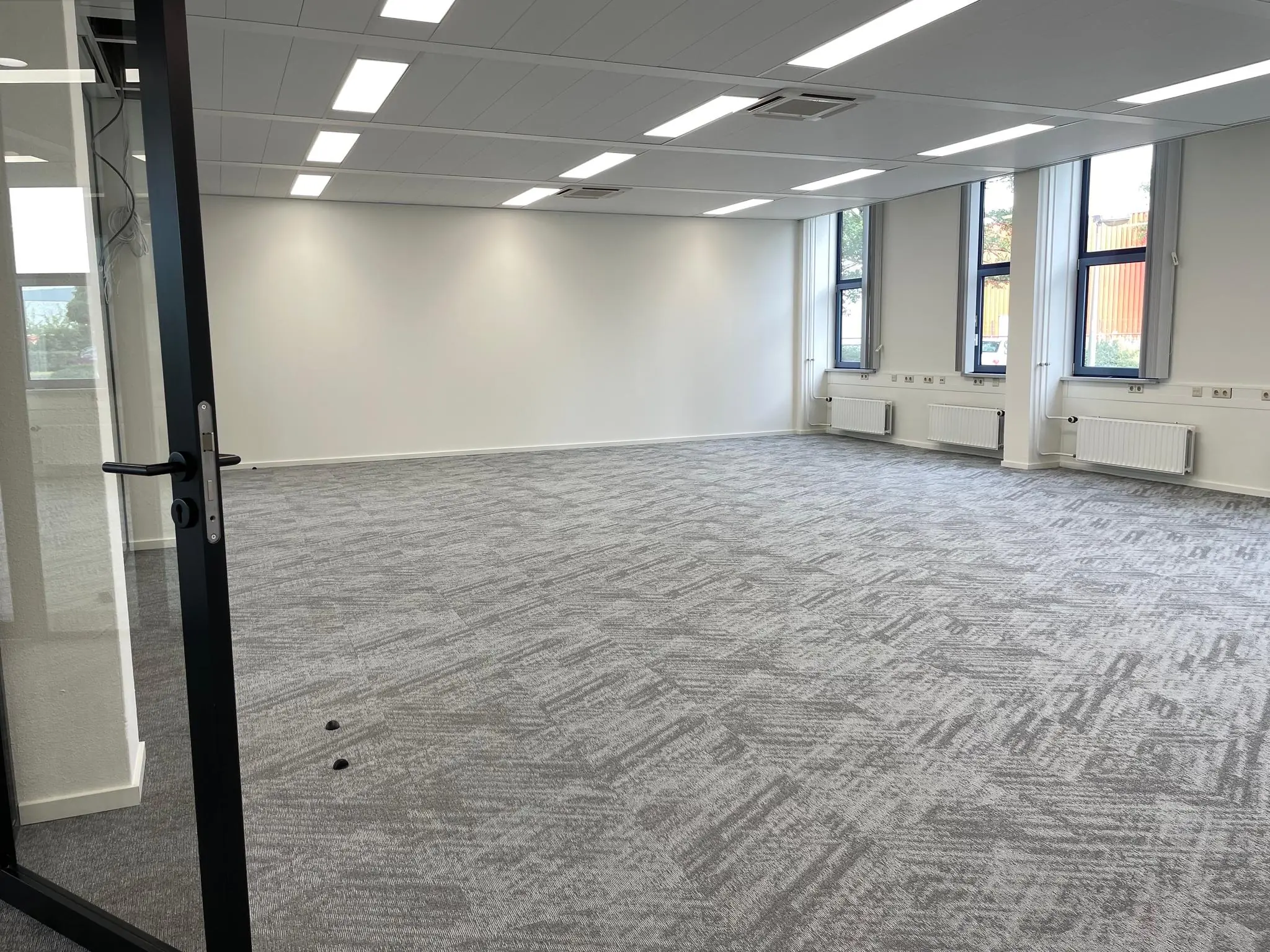 Leeg, modern kantoor met grijze vloerbedekking, witte muren en meerdere ramen aan de Kernkade.