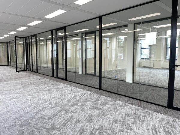 Moderne kantoorruimte aan de Kernkade met glazen scheidingswanden en grijs tapijt.