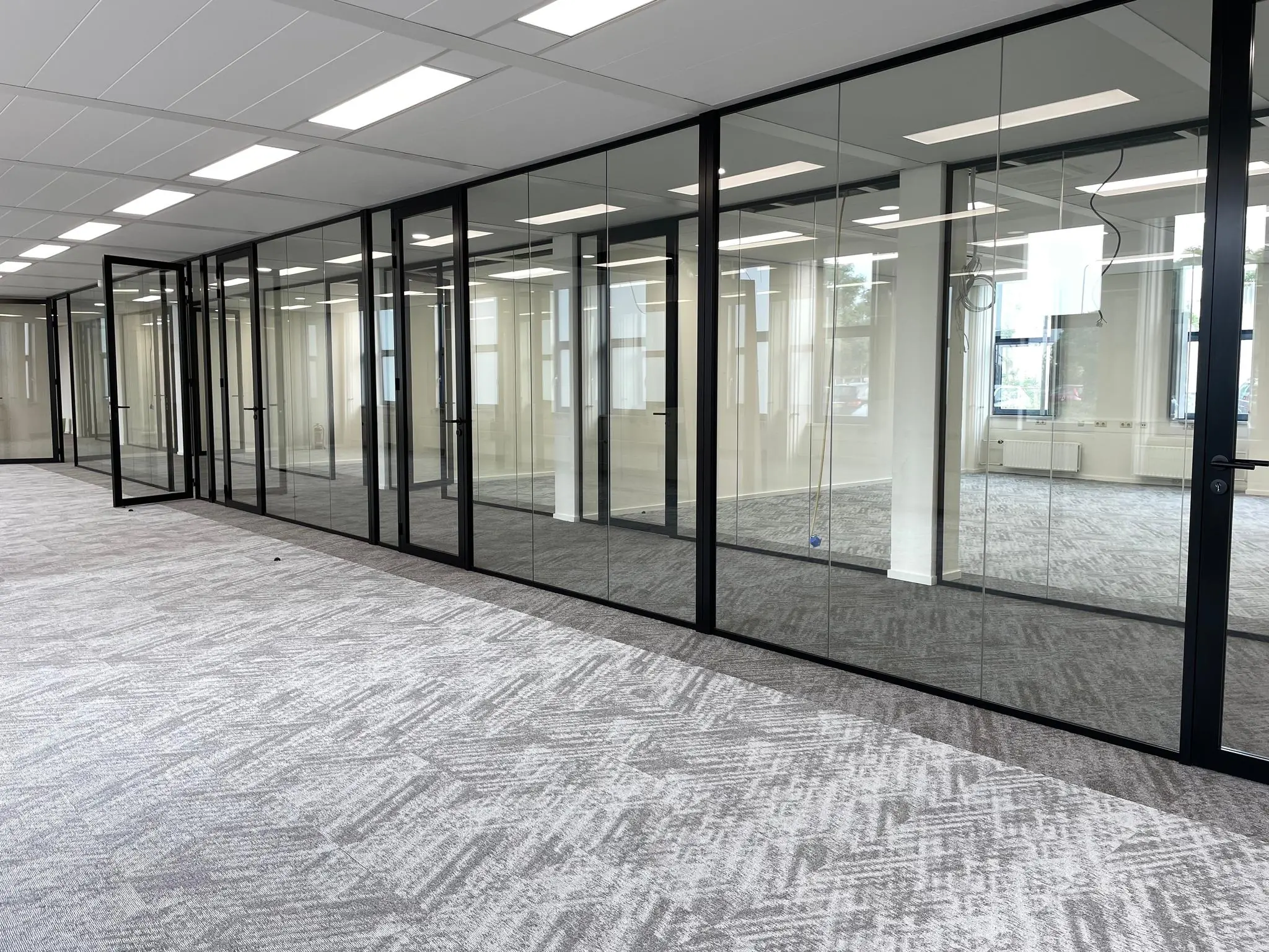 Moderne kantoorruimte aan de Kernkade met glazen scheidingswanden en grijs tapijt.