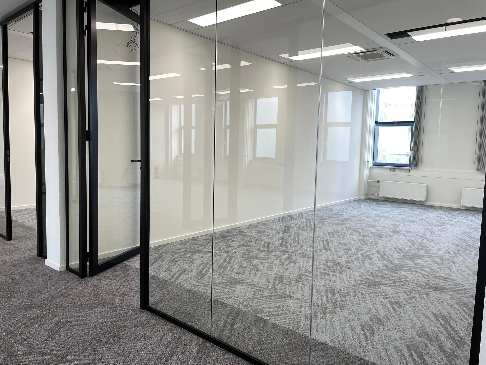 Modern, licht kantoorinterieur aan de Kernkade met glazen wanden en grijs tapijt.