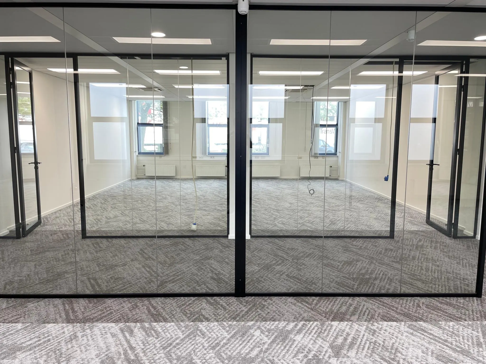 Moderne kantoorruimte aan de Kernkade met glazen wanden, grijs tapijt en uitzicht op ramen aan de straatzijde.