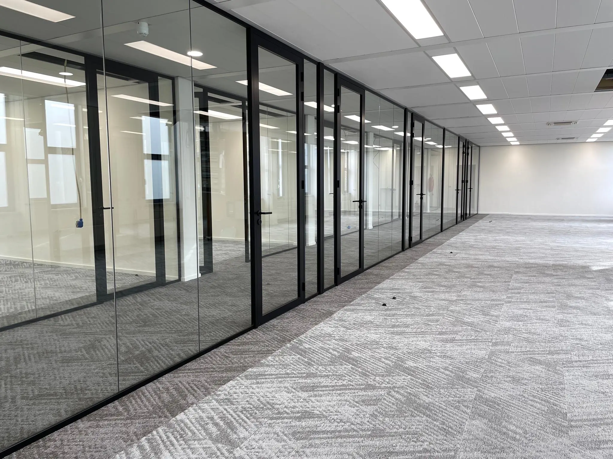 Modern, leeg kantoorgebouw aan de Kernkade met glazen vergaderruimtes en grijs tapijt.