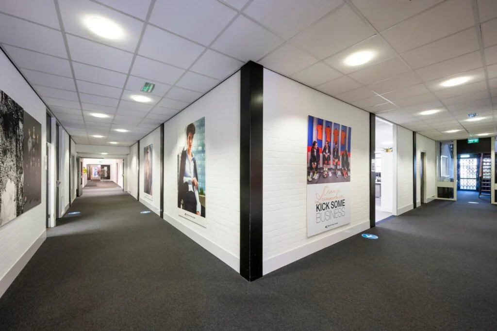 Moderne kantoorhal in Stammerhove met witte muren, grijze vloerbedekking en grote posters aan de wanden.