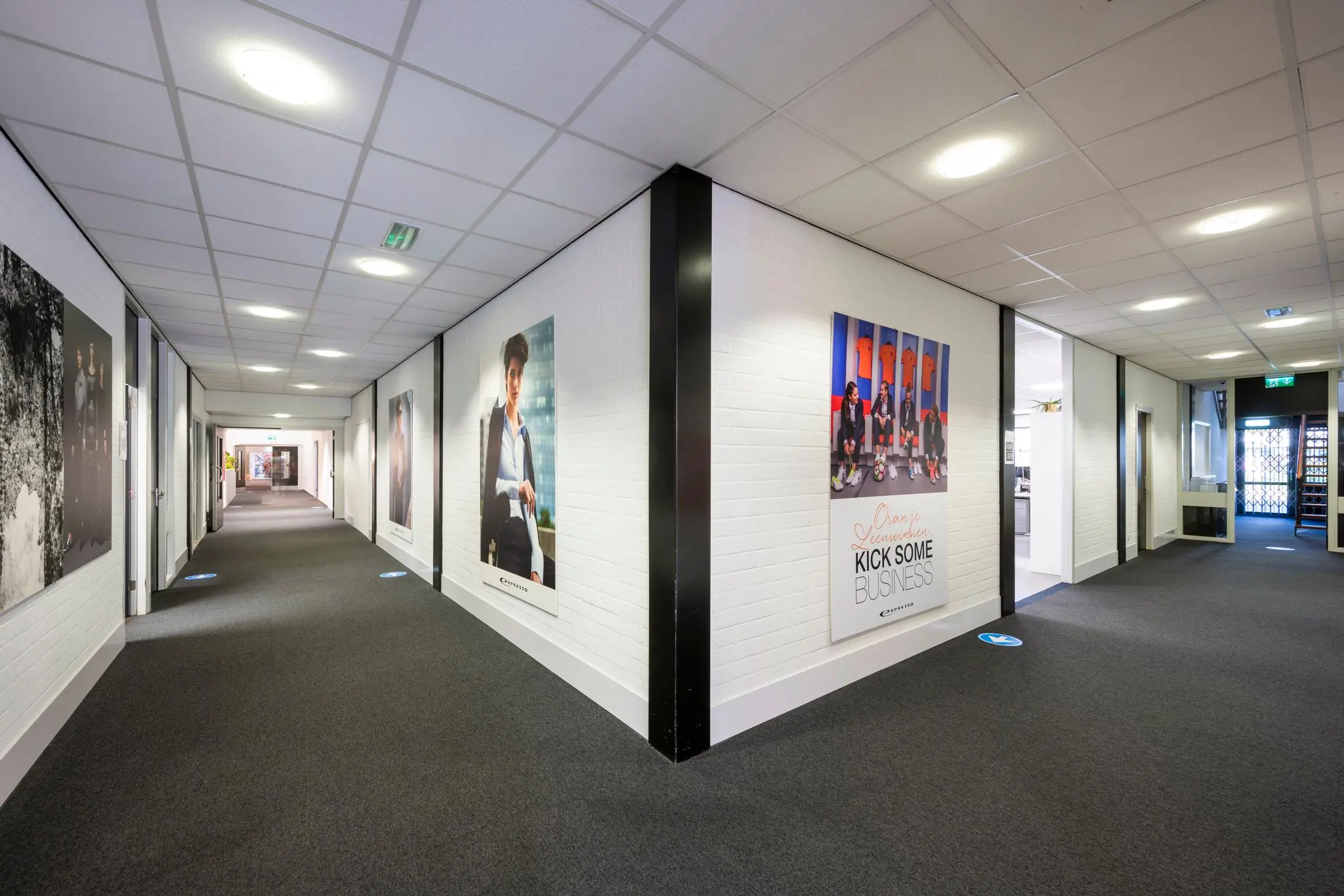 Moderne kantoorhal in Stammerhove met witte muren, grijze vloerbedekking en grote posters aan de wanden.