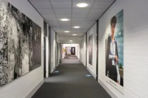 Een verlicht kantoorgebouwgang met grote modeposters aan de muren, waaronder een Expresso-reclame.