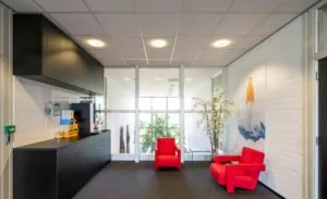 Wachtruimte met een koffiemeubel, twee felrode stoelen, een glazen bijzettafel en een kunstwerk aan de muur bij Stammerhove.