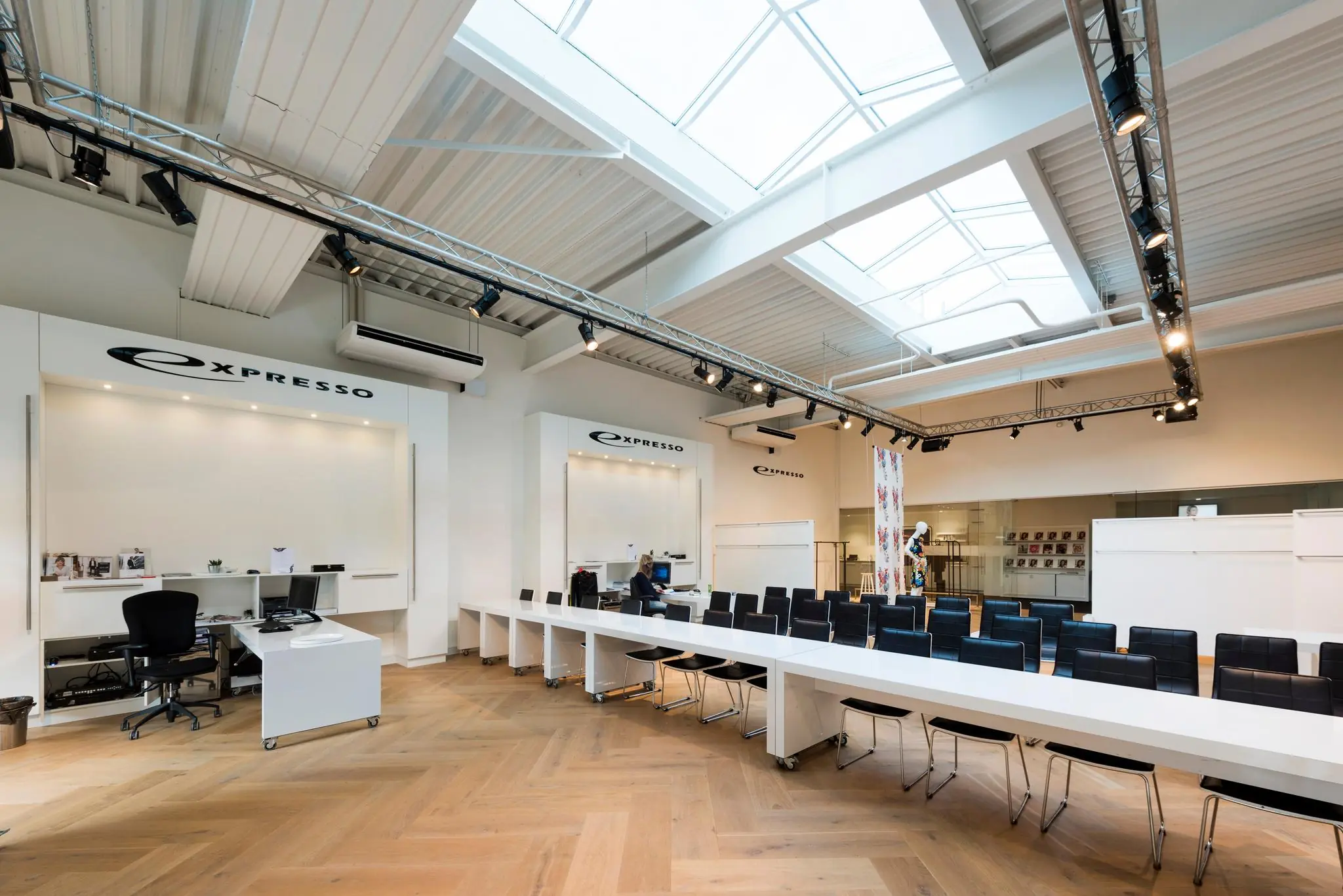 Modern ingerichte showroom van Expresso met lange witte tafels, zwarte stoelen en een glazen dak.